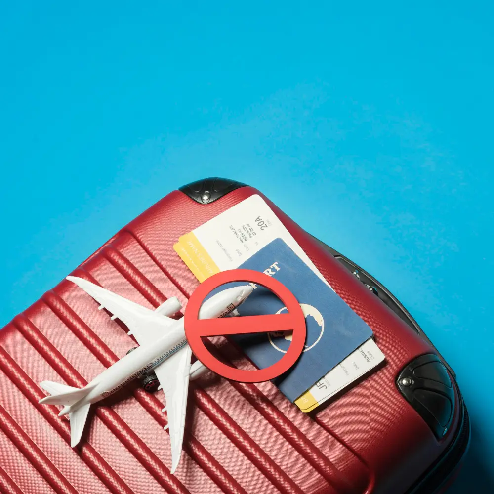 A imagem tem um fundo azul e uma mala vermelha. Em cima da mala tem um avião, passaporte, passagens e um sinal de proibido.